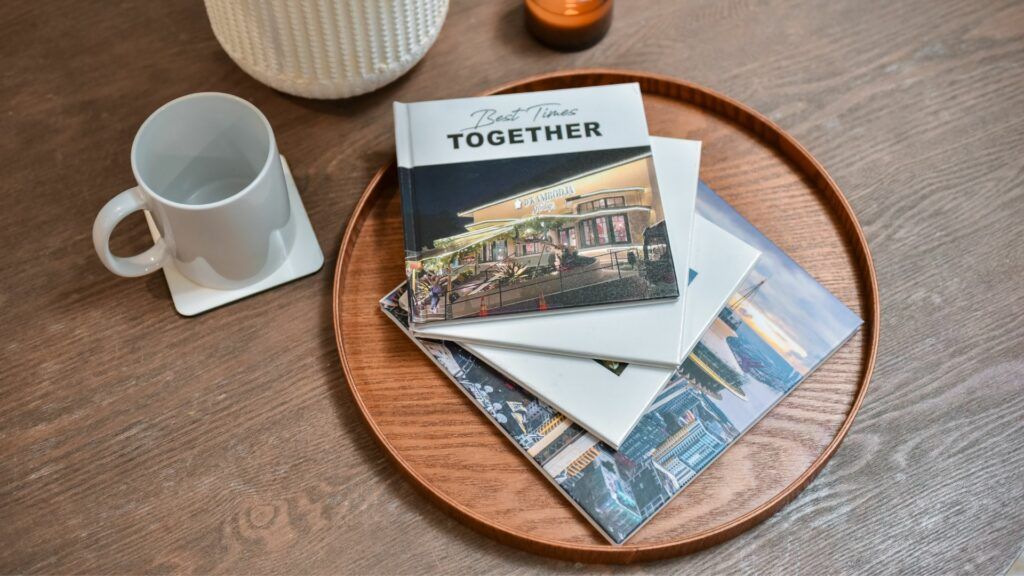 Photo books in different sizes stacked on a round wooden tray beside a mug and a candle