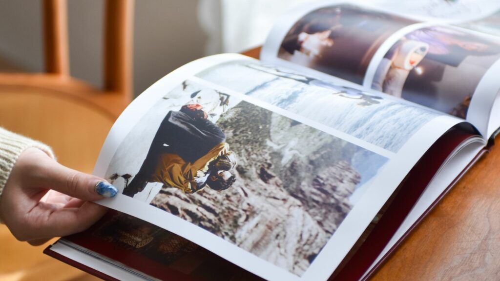 Hand flipping through a printed travel photo book with large photos running across the pages