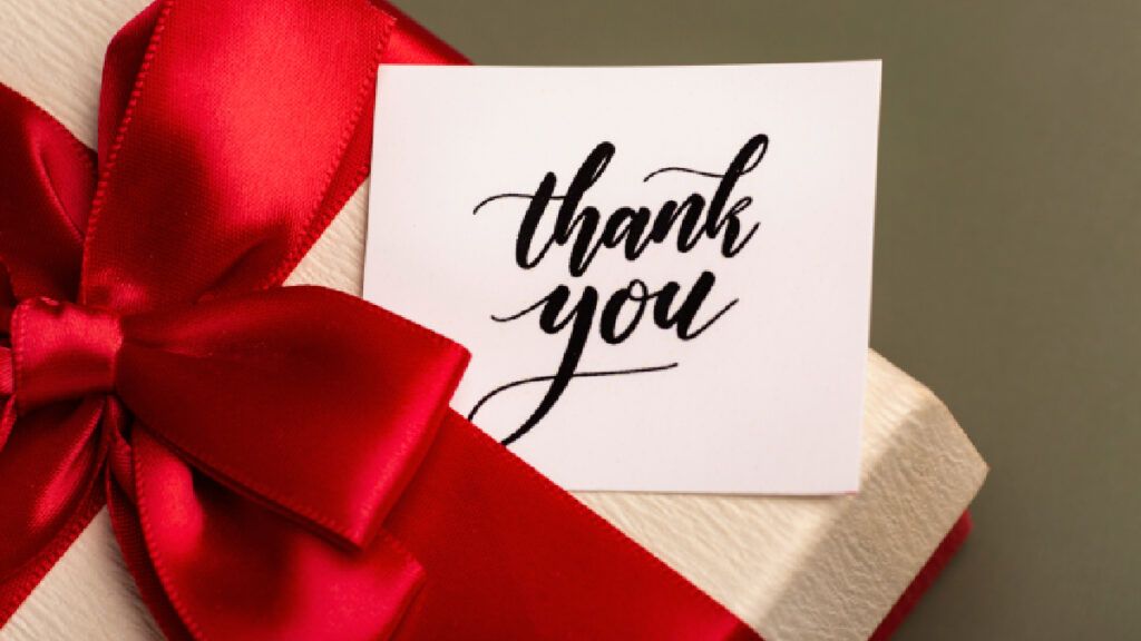 Handwritten thank you card tucked into a gift box tied with a red satin ribbon